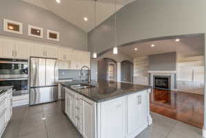 Spacious kitchen featuring an expansive center island with a double basin sink and dark stone countertop, white cabinetry with brushed nickel hardware, stainless steel appliances, and tile flooring