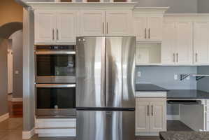 Kitchen featuring stainless steel appliances, white cabinetry, dark countertops, and a double wall oven
