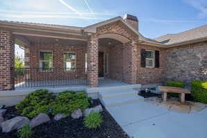 Brick and stone exterior featuring an arched entry, covered porch with black metal railing, and a window with black louvered shutters