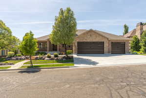 Brick and stone veneer exterior with a multi-car garage, concrete driveway, and a front yard featuring mature trees and decorative rock landscaping