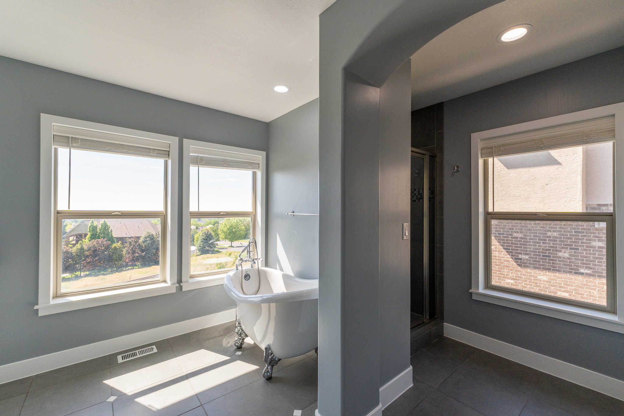 Freestanding clawfoot tub featuring chrome fixtures, set against multiple large windows with white trim