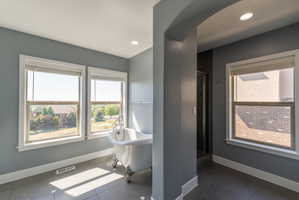 Freestanding clawfoot tub featuring chrome fixtures, set against multiple large windows with white trim