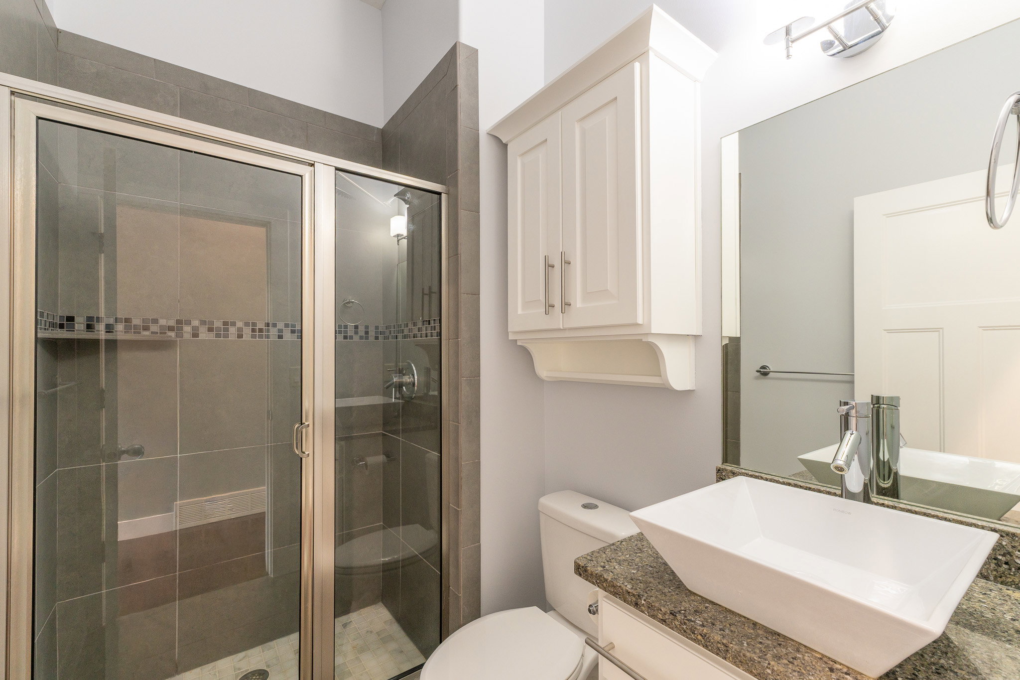 Modern bathroom featuring a rectangular vessel sink, granite-finish countertop, and white shaker-style cabinetry
