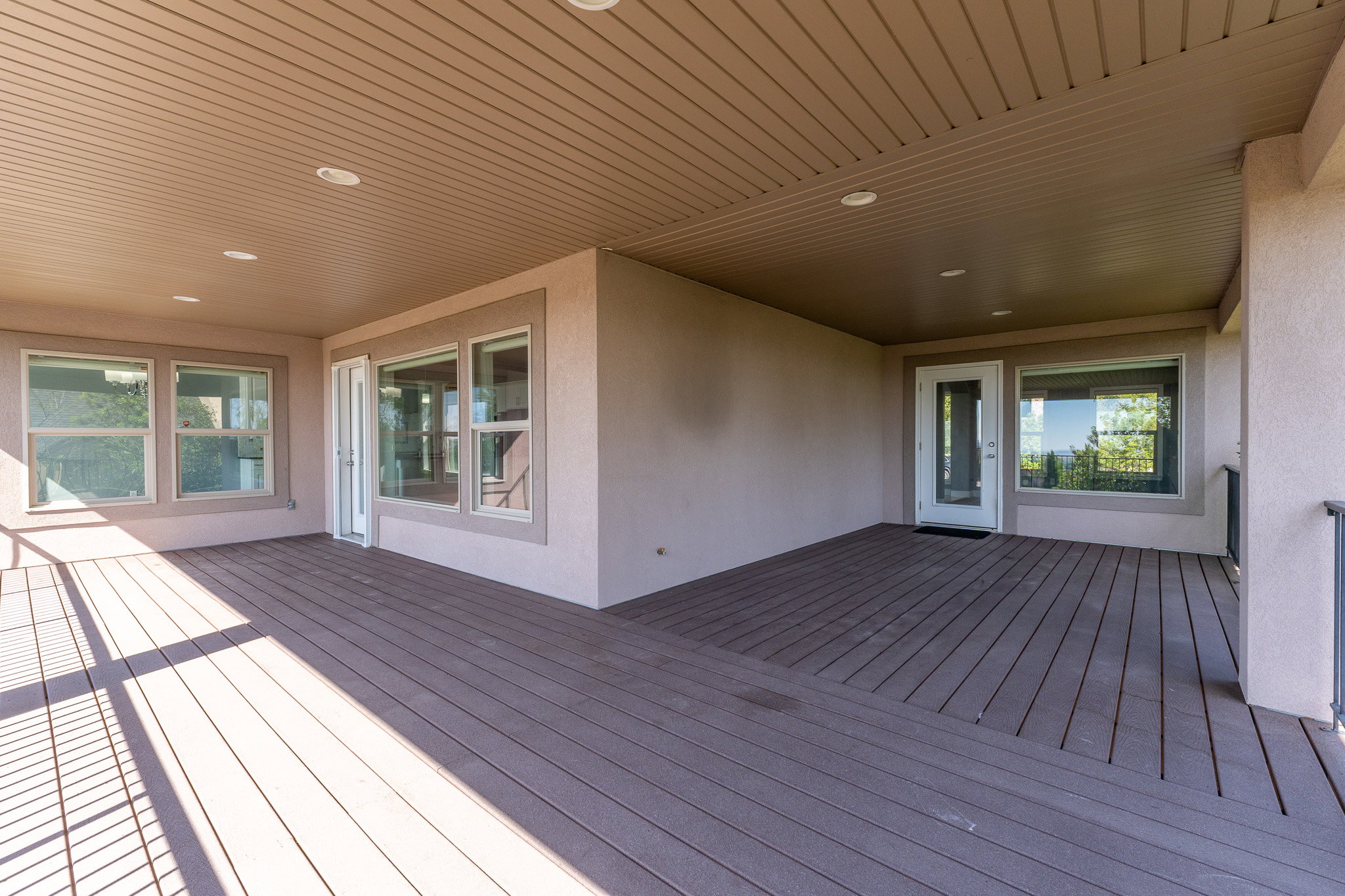 Expansive covered deck featuring composite decking, recessed lighting, and multiple large windows