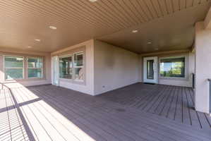Expansive covered deck featuring composite decking, recessed lighting, and multiple large windows