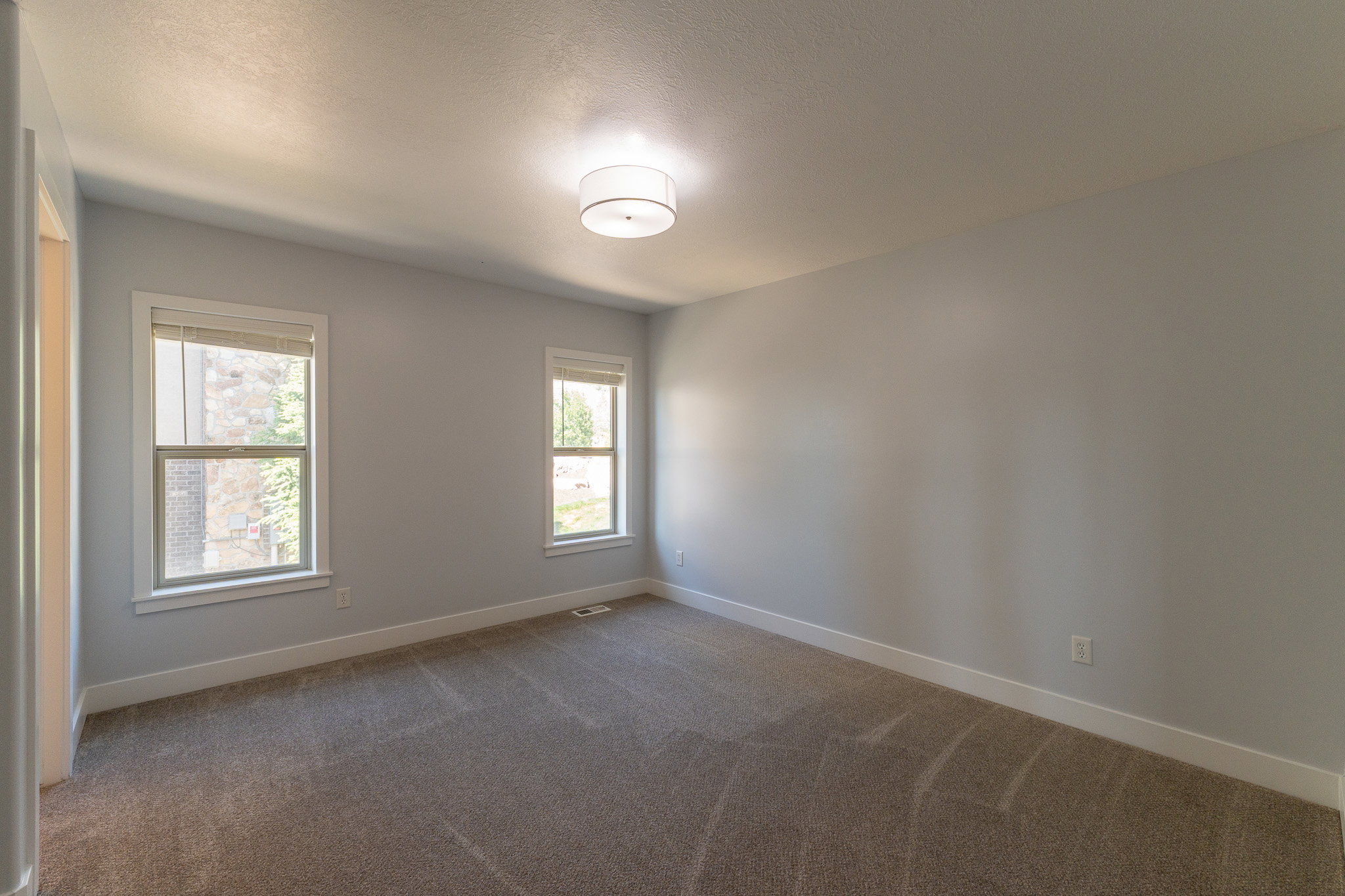 Neutral-toned room featuring two framed windows, plush carpeting, a ceiling-mounted light fixture, and white baseboards