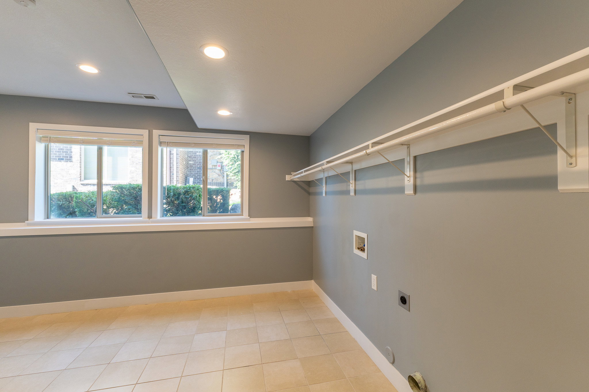 Laundry room featuring tile flooring, dual windows, recessed lighting, and wall-mounted shelving with hanging rods