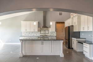 Spacious kitchen featuring a central island with dark countertops, white cabinetry, a stainless steel range hood, pendant lighting, and a patterned tile backsplash