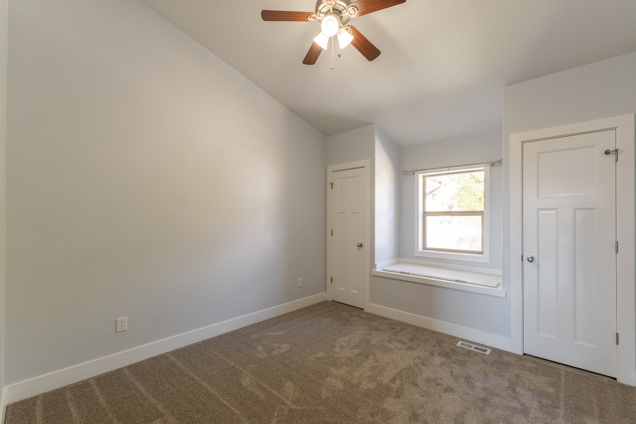 Carpeted room featuring a window with a built-in window seat, a ceiling fan with light fixture, and two panel doors