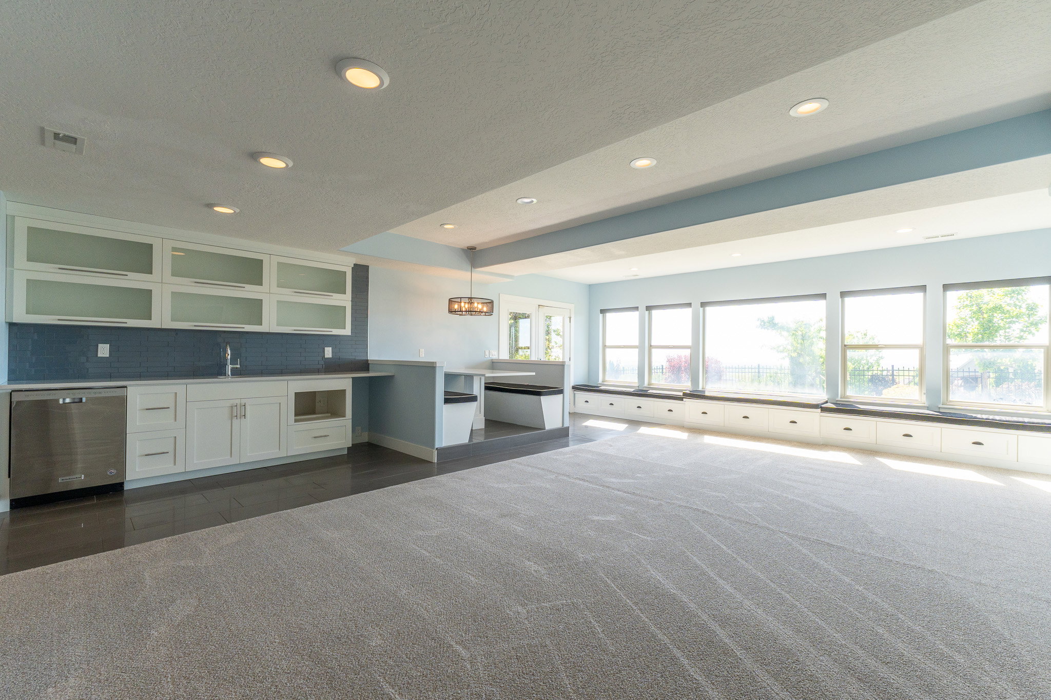 Spacious recreational room featuring a wet bar with built-in cabinetry, an integrated stainless steel dishwasher, and a tile backsplash