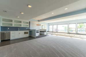 Spacious recreational room featuring a wet bar with built-in cabinetry, an integrated stainless steel dishwasher, and a tile backsplash