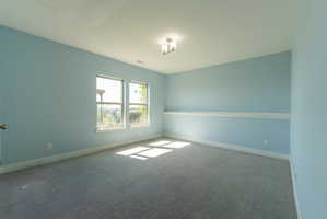 Bright room featuring two windows, light blue walls, gray textured carpet, white baseboards, and a contemporary ceiling fixture