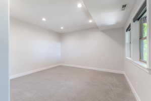 Spacious room featuring light gray carpeting, recessed ceiling lighting, and multiple windows with roller shades