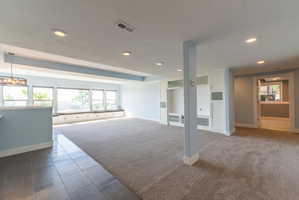 Expansive living area featuring a built-in window seat with storage, wall-to-wall carpeting, recessed lighting, and a built-in media center with glass-front cabinetry