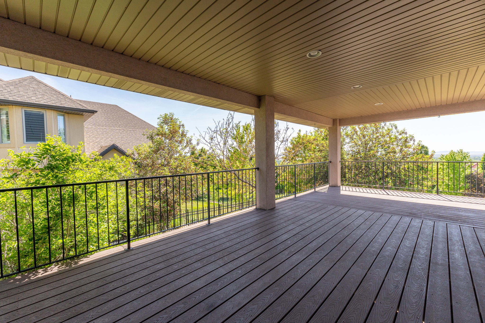Spacious covered deck featuring composite decking, recessed lighting, and black metal railings, offering an outdoor extension of living space