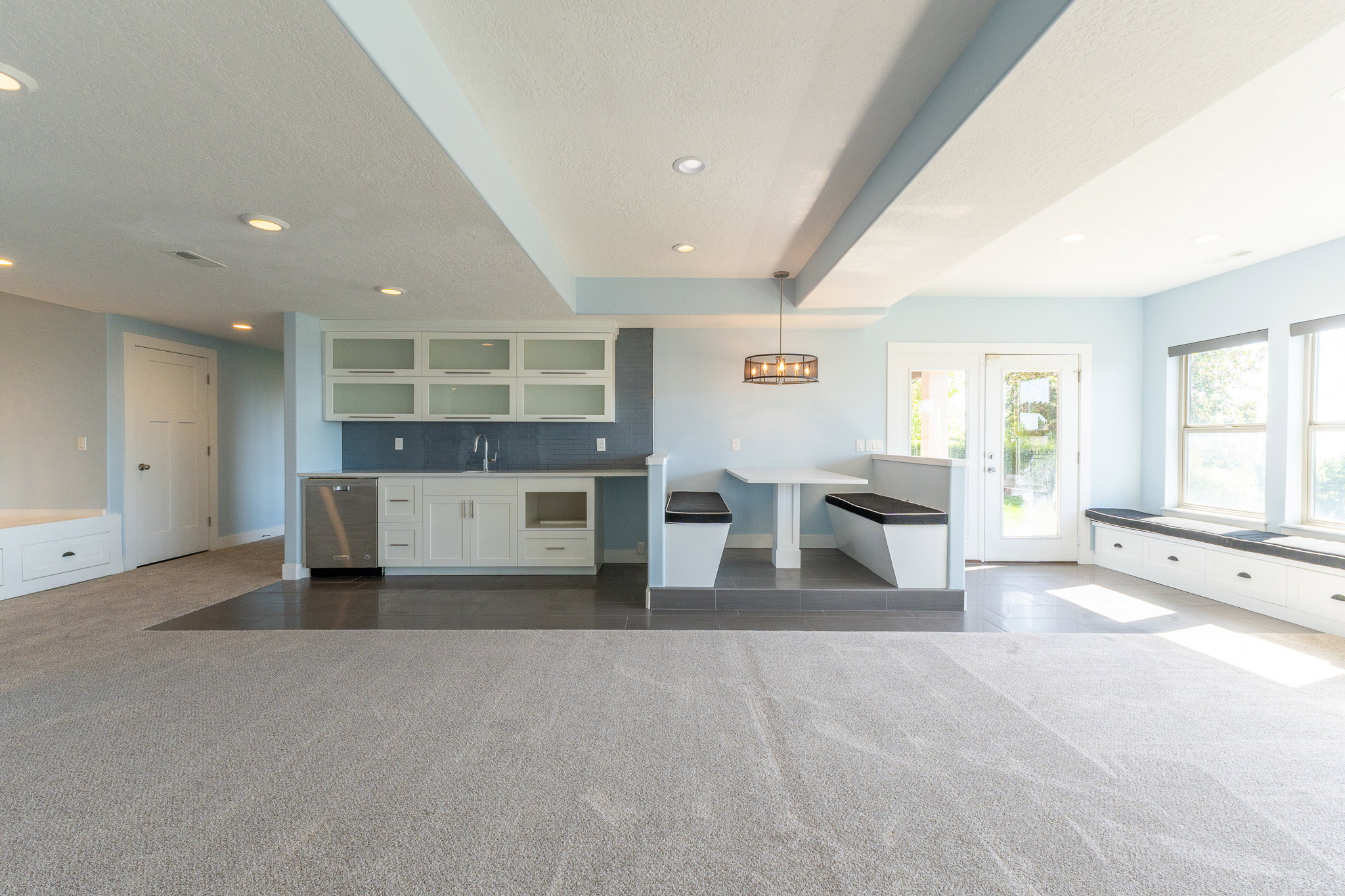 Spacious room featuring light gray carpeting and a wet bar with white cabinetry and a stainless steel dishwasher