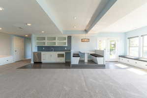 Spacious room featuring light gray carpeting and a wet bar with white cabinetry and a stainless steel dishwasher