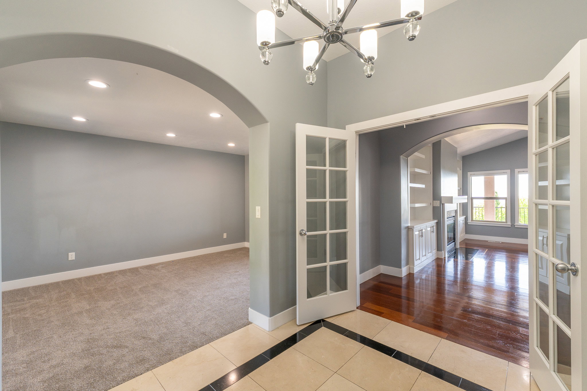 Entryway featuring tile flooring with a dark border accent, leading to an arched opening and double French doors
