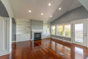 Spacious living area featuring rich wood-finish flooring, a vaulted ceiling with recessed lighting, and a modern fireplace with a tiled surround