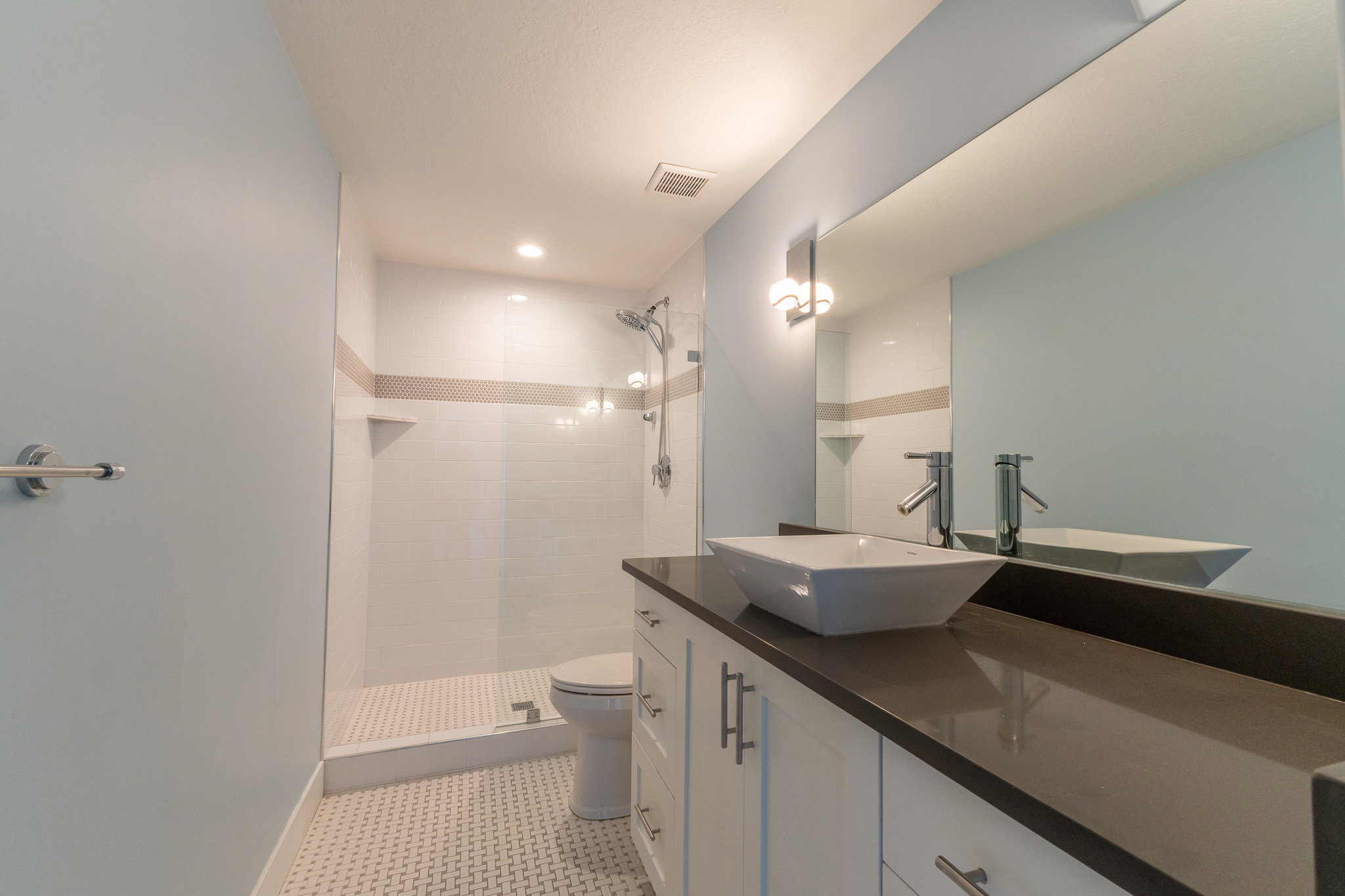 Modern bathroom featuring a vanity with a vessel sink, dark countertop, and white cabinetry