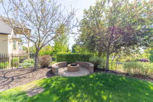 Outdoor fire pit with a brick-paver base and curved stone retaining walls, surrounded by mature trees and landscaping