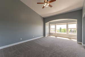 Spacious room with arched architectural detail, featuring a trio of large windows with white trim, a ceiling fan, and grey carpeting
