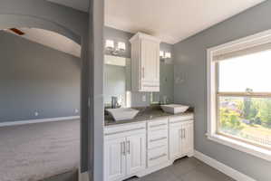 Dual vessel sinks set on a granite-finish countertop with white cabinetry, illuminated by two vanity light fixtures