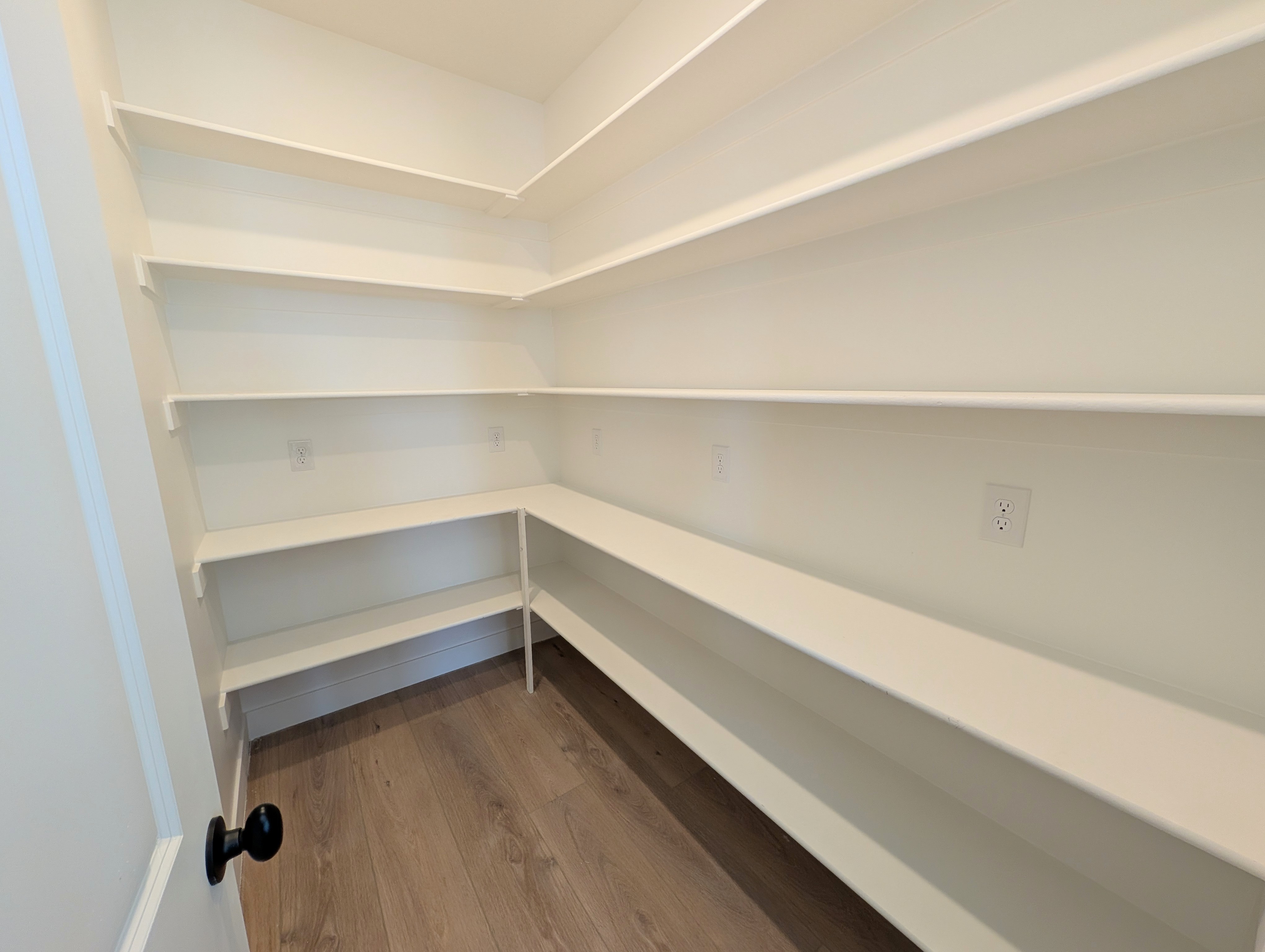 Walk-in pantry featuring extensive white shelving, wood-finish flooring, and multiple electrical outlets