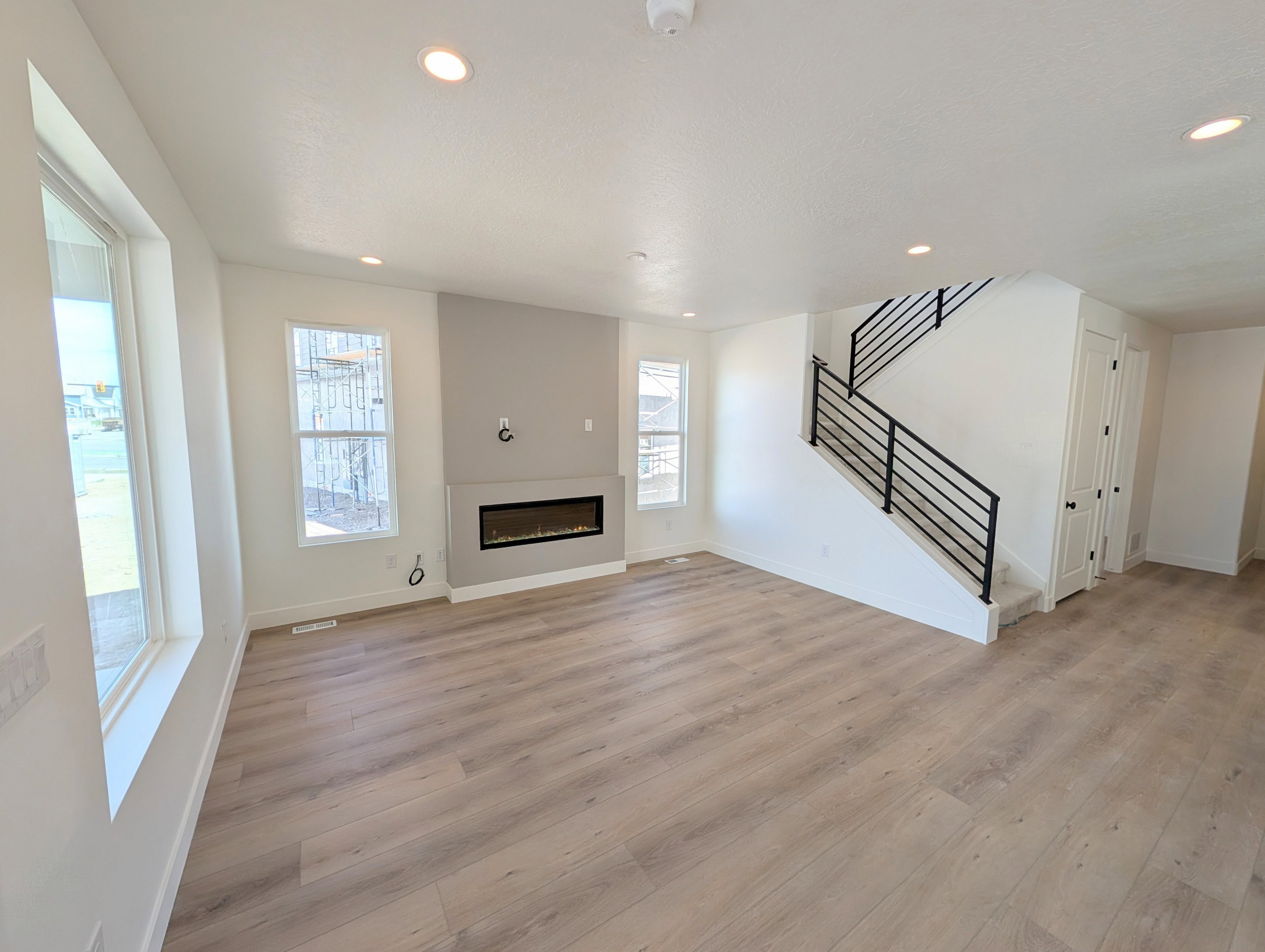 Spacious living area featuring wood-finish flooring, a modern electric fireplace with a gray accent wall, recessed lighting, and large windows