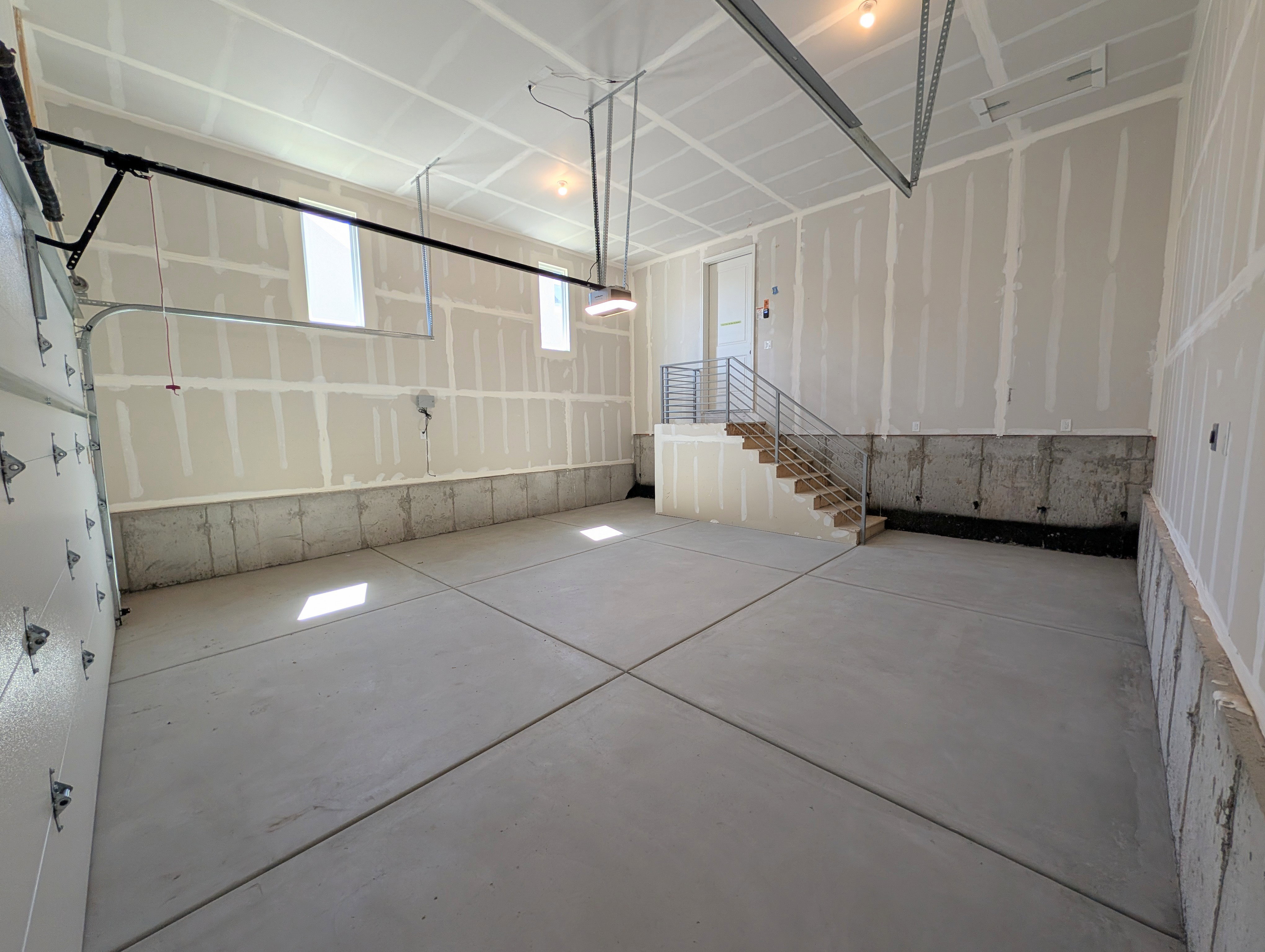 Spacious garage with concrete flooring, natural light through multiple windows, and a built-in staircase featuring metal railings