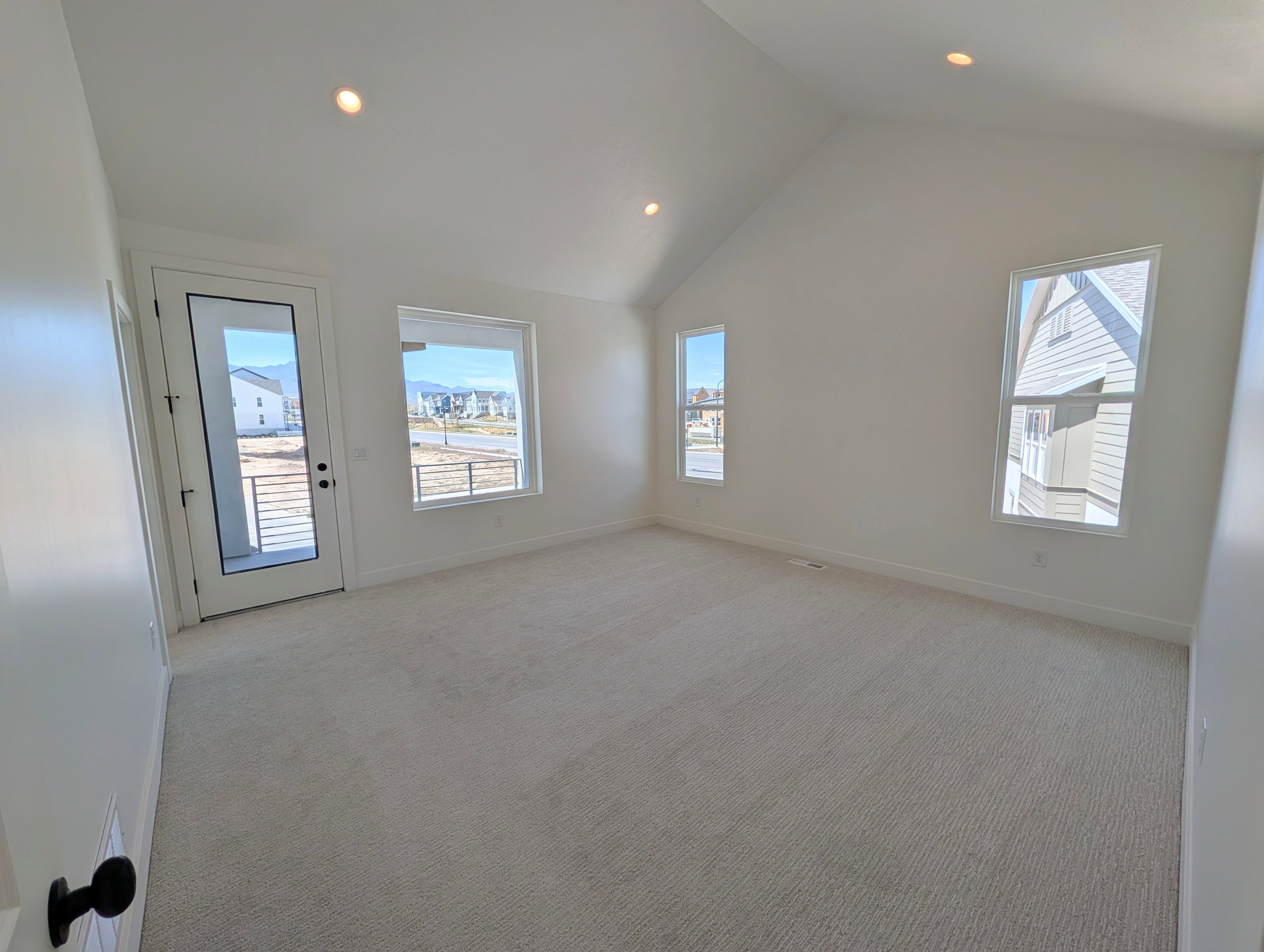 Primary bedroom featuring access to private balcony, vaulted ceilings, recessed lighting, neutral carpet flooring, and multiple windows providing ample natural light