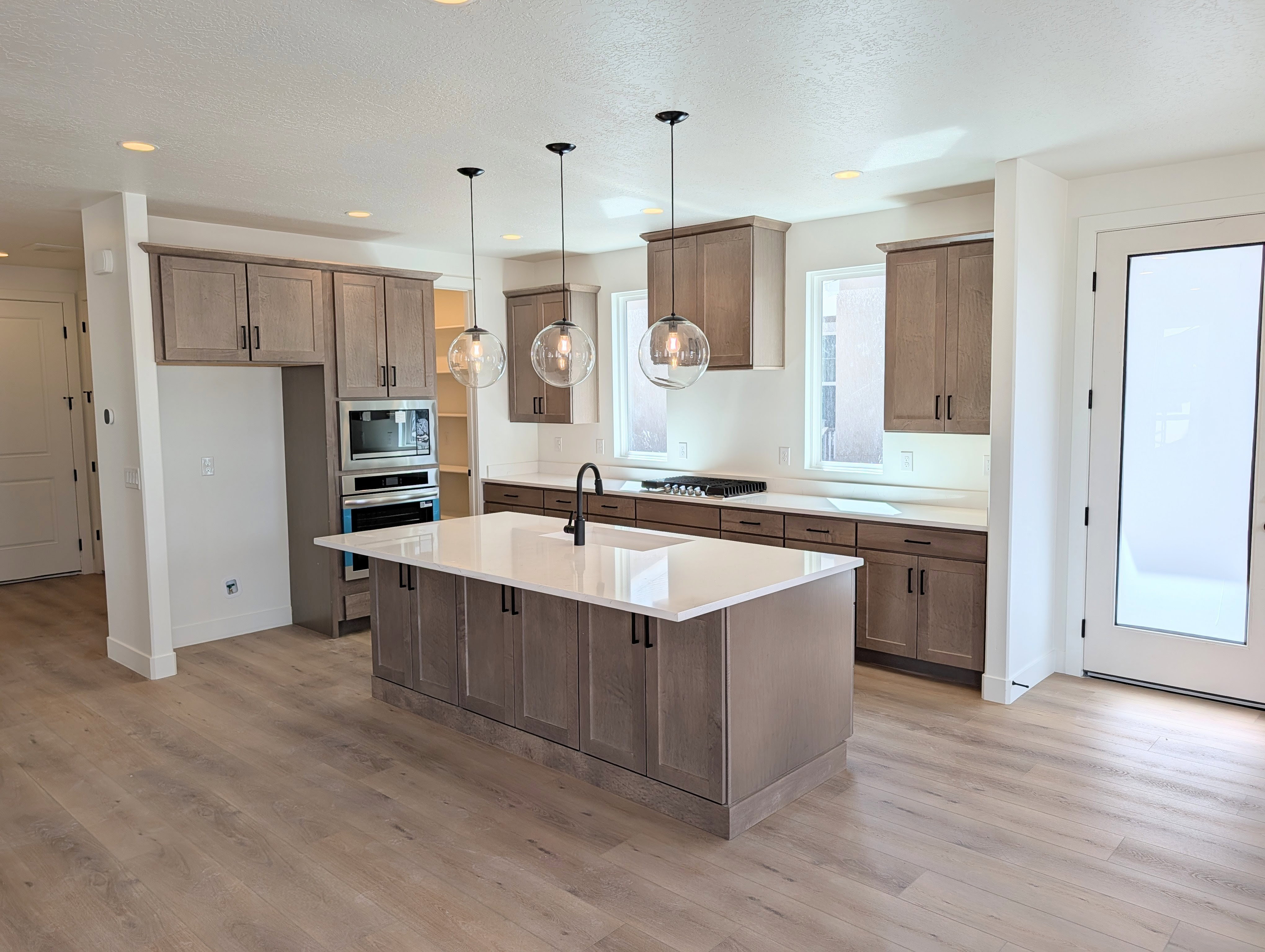 Open-concept kitchen featuring an oversized island with an integrated sink, shaker-style cabinetry, stainless steel appliances, and wood-finish flooring
