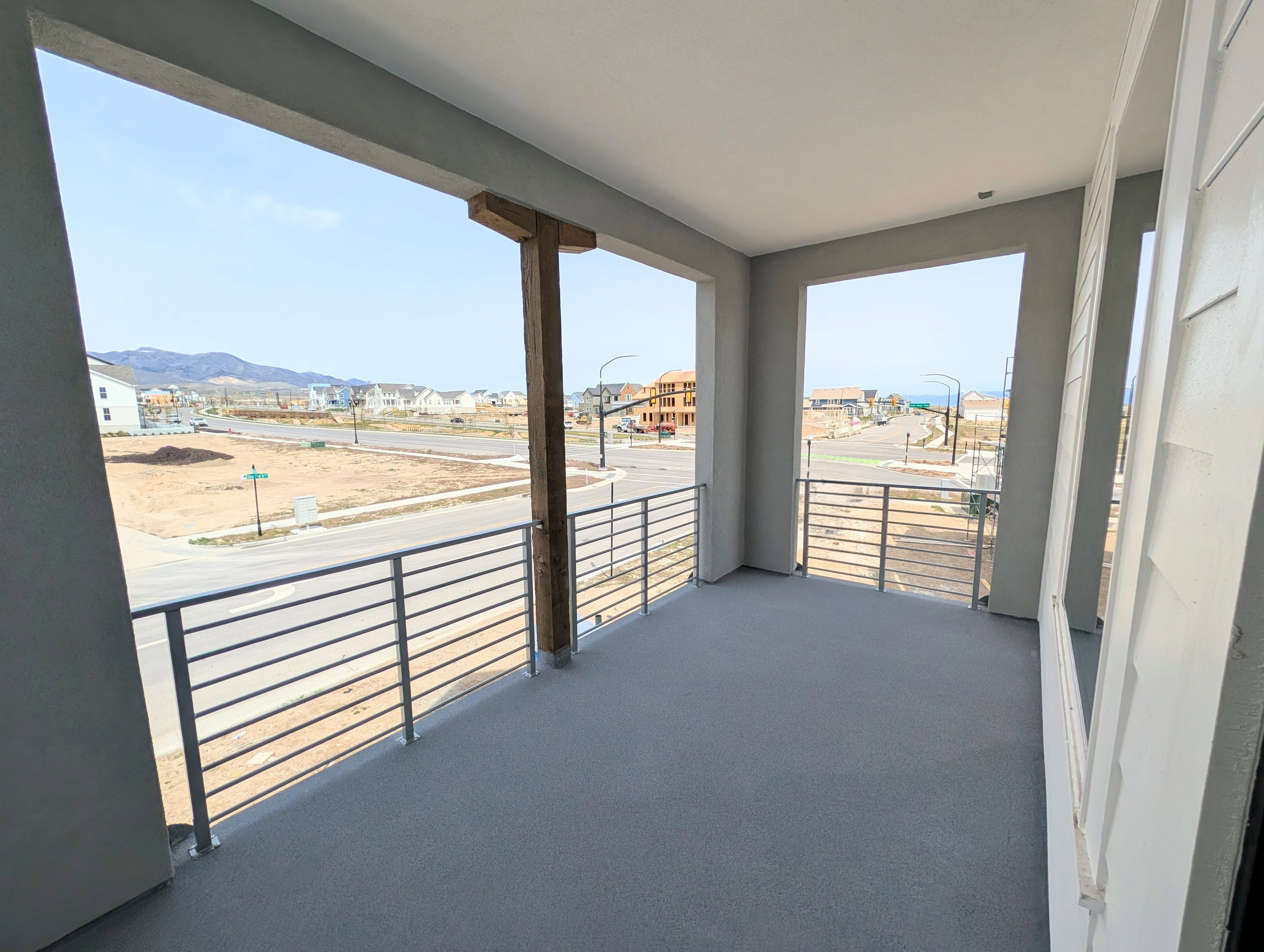 Spacious balcony off of Primary bedroom featuring a durable gray surface, modern horizontal metal railings, and a prominent wood-beam support