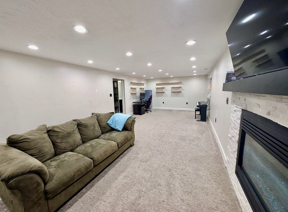 Spacious living area featuring recessed lighting, carpet flooring, a built-in fireplace with a stone surround, and floating wall shelves