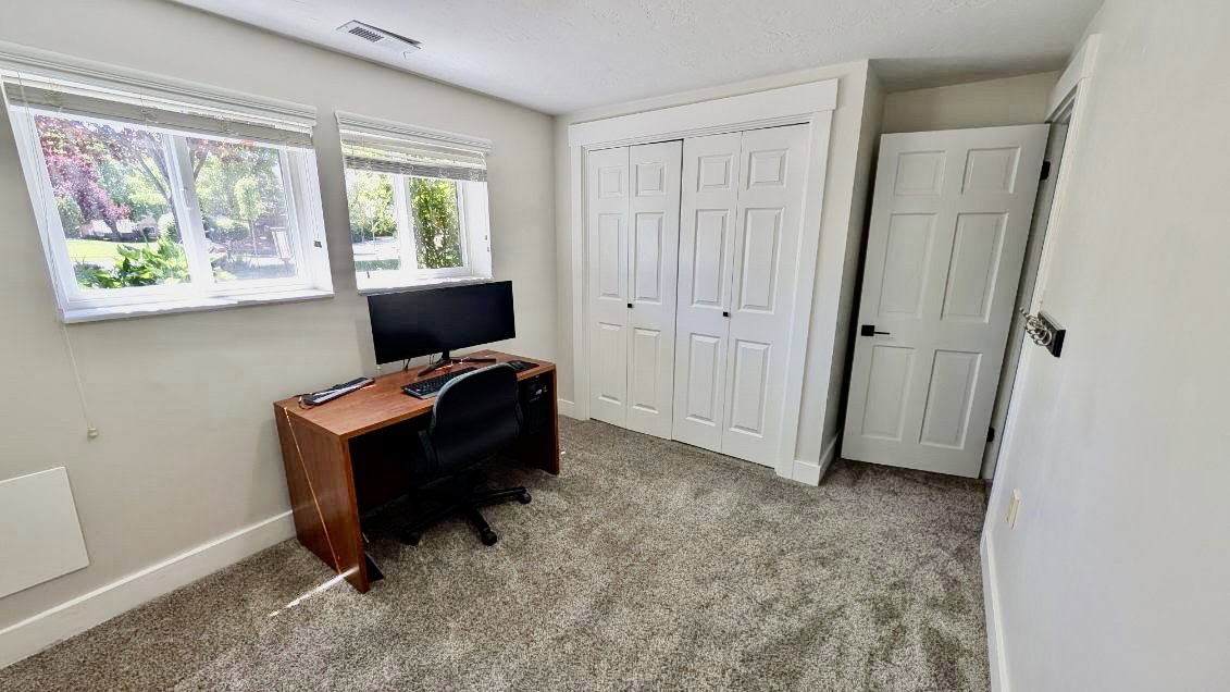 Carpeted room featuring two white-framed windows, white baseboards, and a built-in closet with bi-fold doors