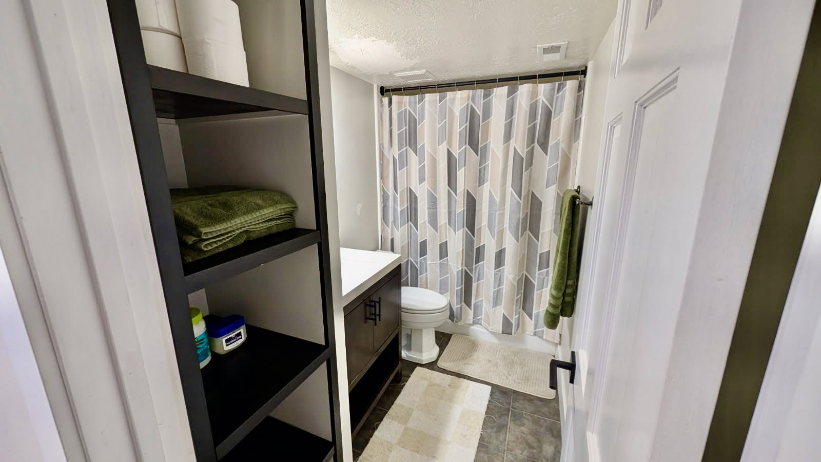 Compact bathroom featuring a dark wood-finish vanity with a white countertop and a geometric pattern shower curtain