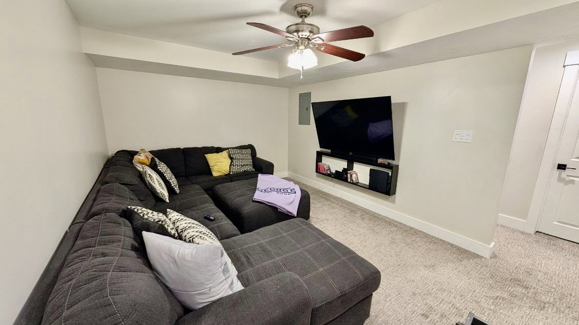 Carpeted recreation room featuring a recessed ceiling, ceiling fan with light fixture, and a wall-mounted entertainment shelf