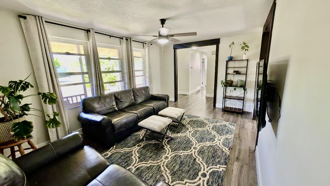 Living area featuring wood-finish flooring, a ceiling fan with integrated lighting, and white walls