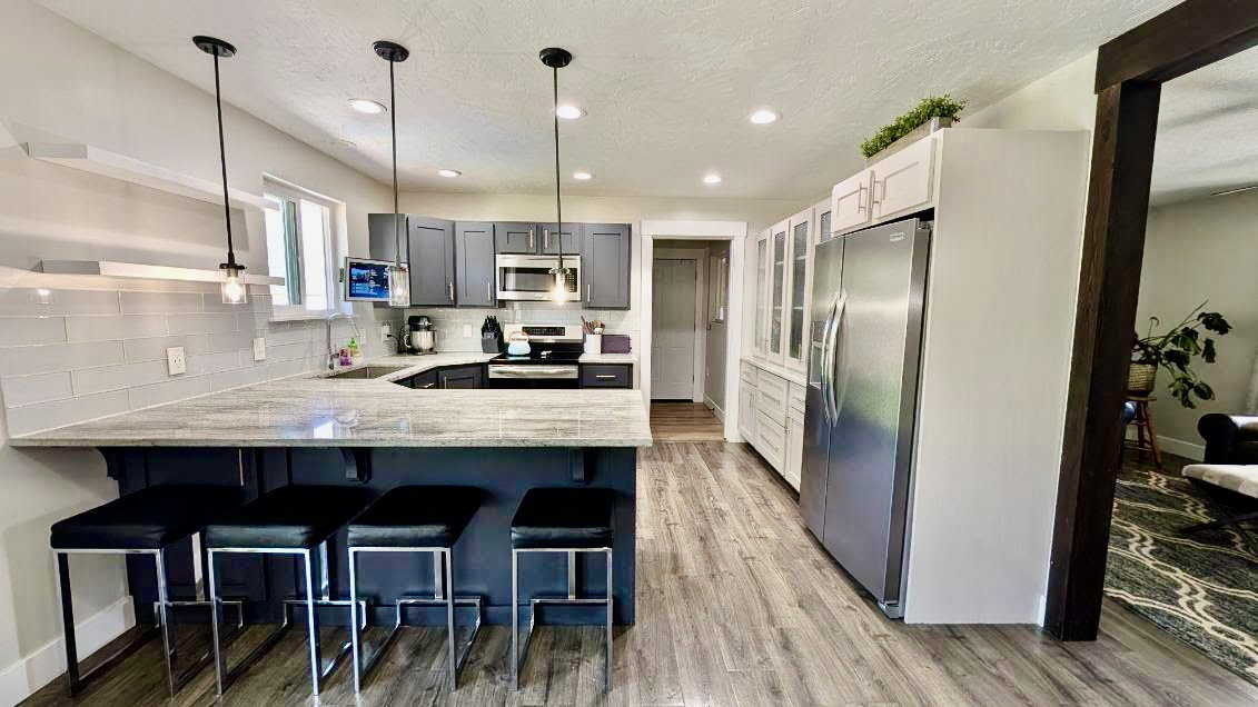 Modern kitchen featuring a breakfast bar with seating, gray cabinetry, light-toned countertops, and stainless steel appliances