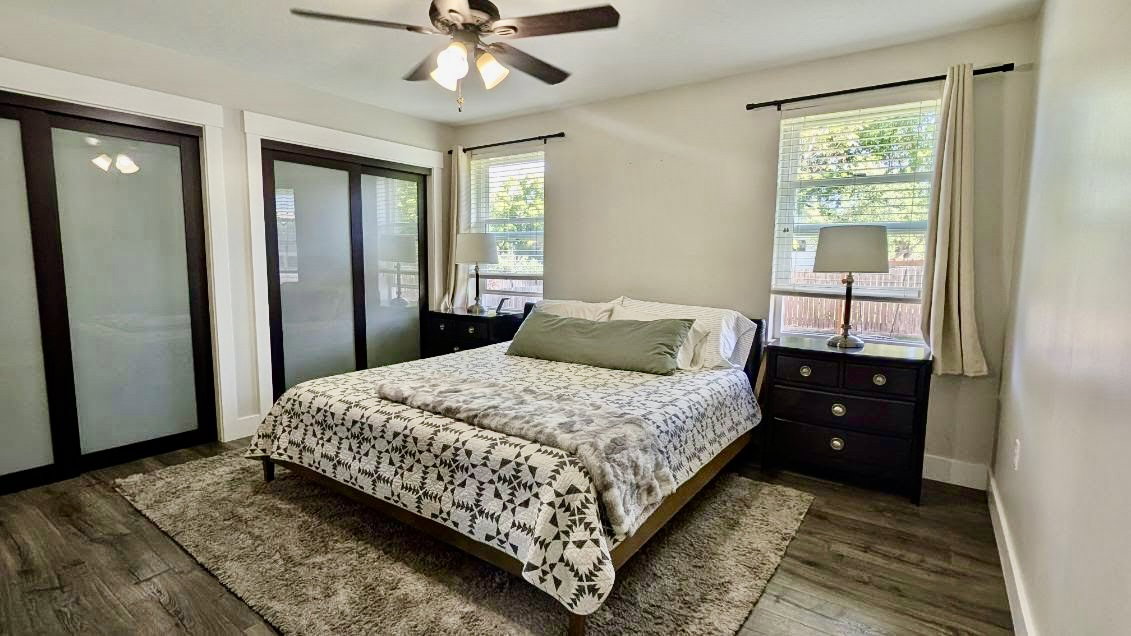 Recessed bedroom featuring wood-finish flooring, a ceiling fan, and two windows with blinds