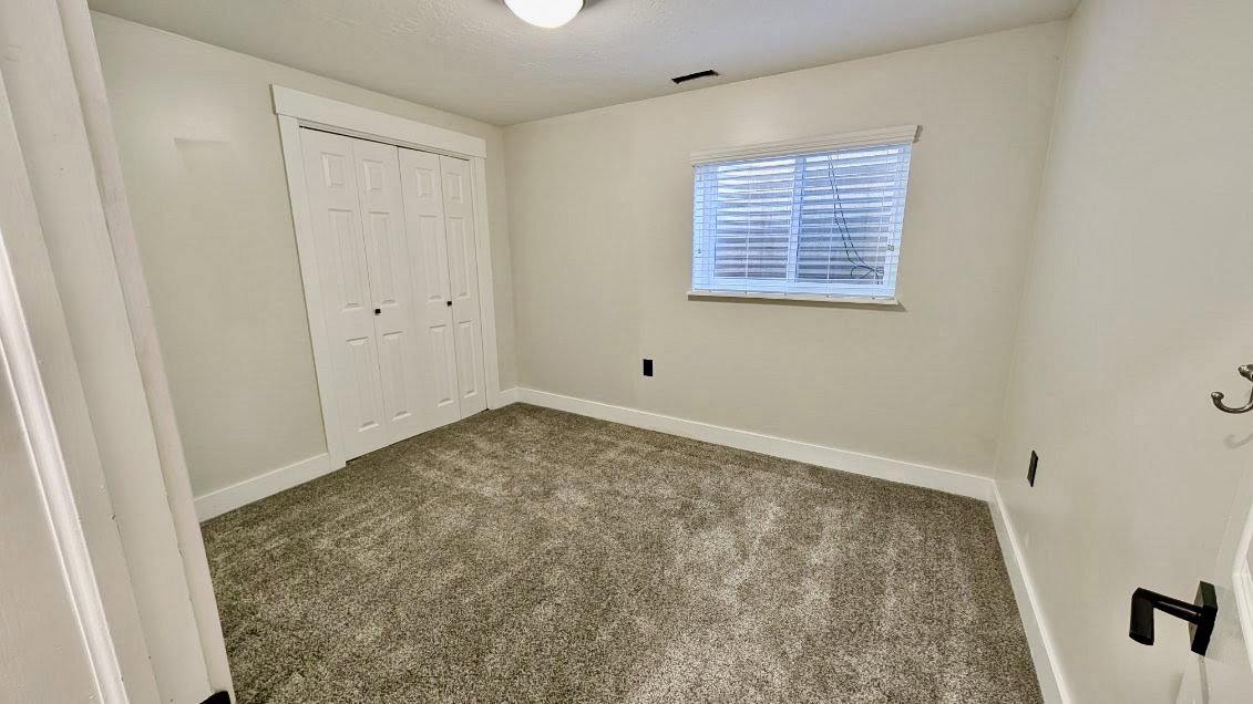 Neutral-toned room featuring a large bi-fold closet, textured carpeting, and a window with blinds