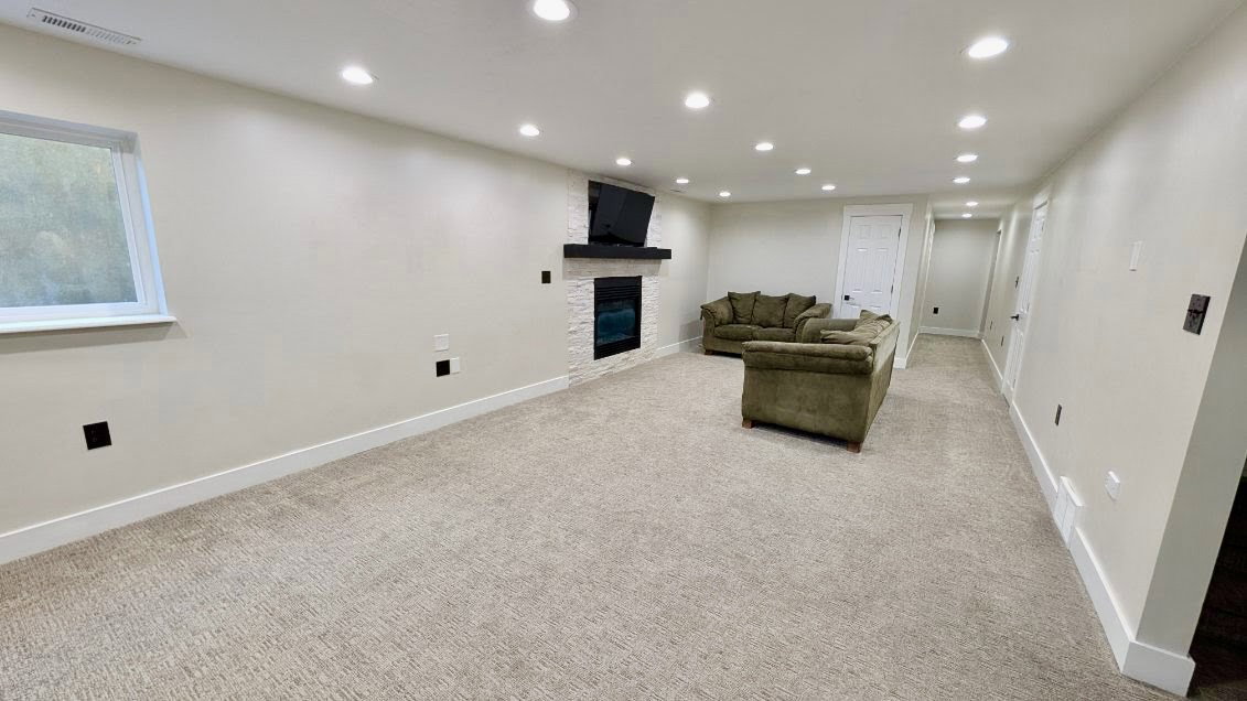 Spacious living area featuring neutral carpeting, recessed lighting, a fireplace with a white stone surround, a dark wood mantel, and white trim throughout