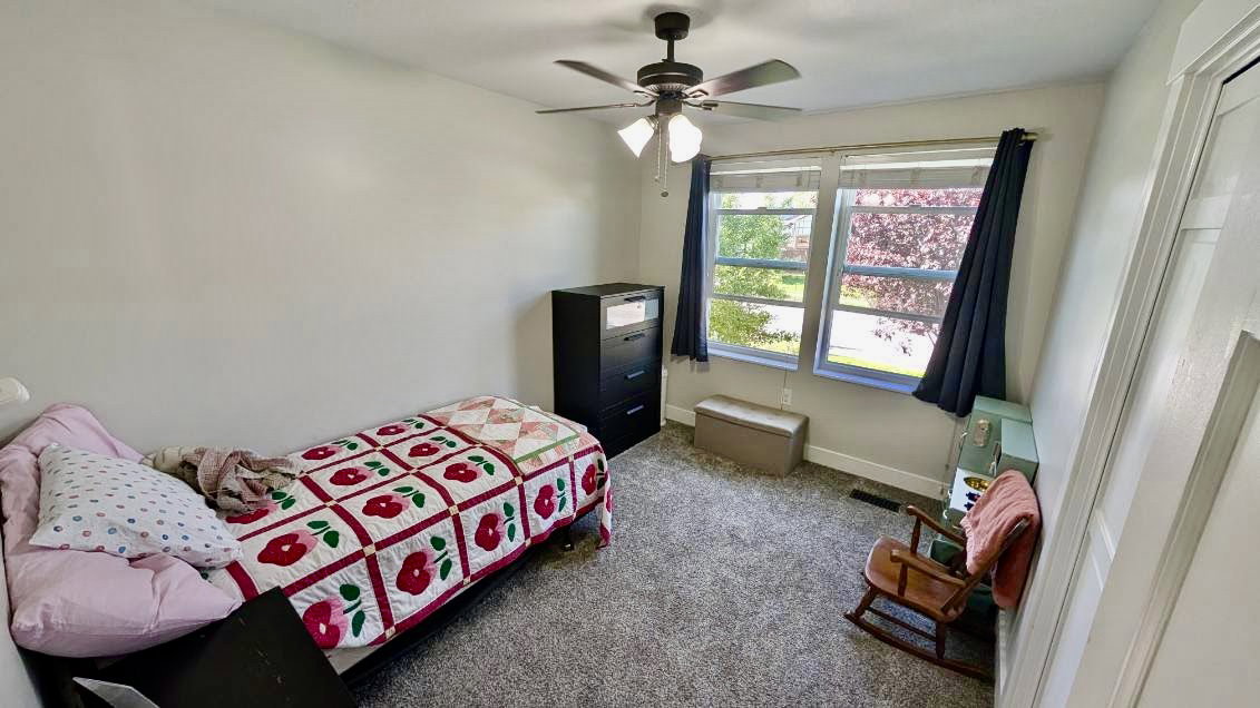 Carpeted room with a ceiling fan light fixture and dual windows