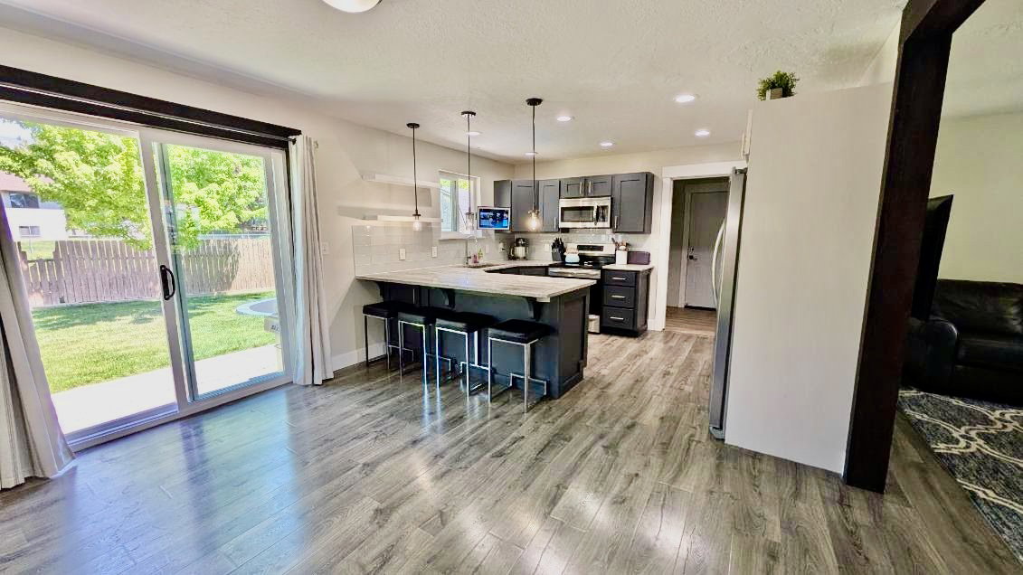 Kitchen featuring dark cabinetry, stainless steel appliances, a center island with pendant lighting, and wood-finish flooring