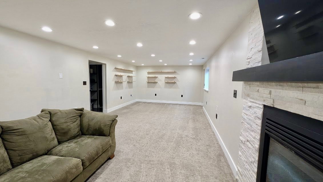 Expansive room featuring recessed lighting, carpet flooring, a built-in fireplace with a stone surround, a black mantle, and floating wood shelves