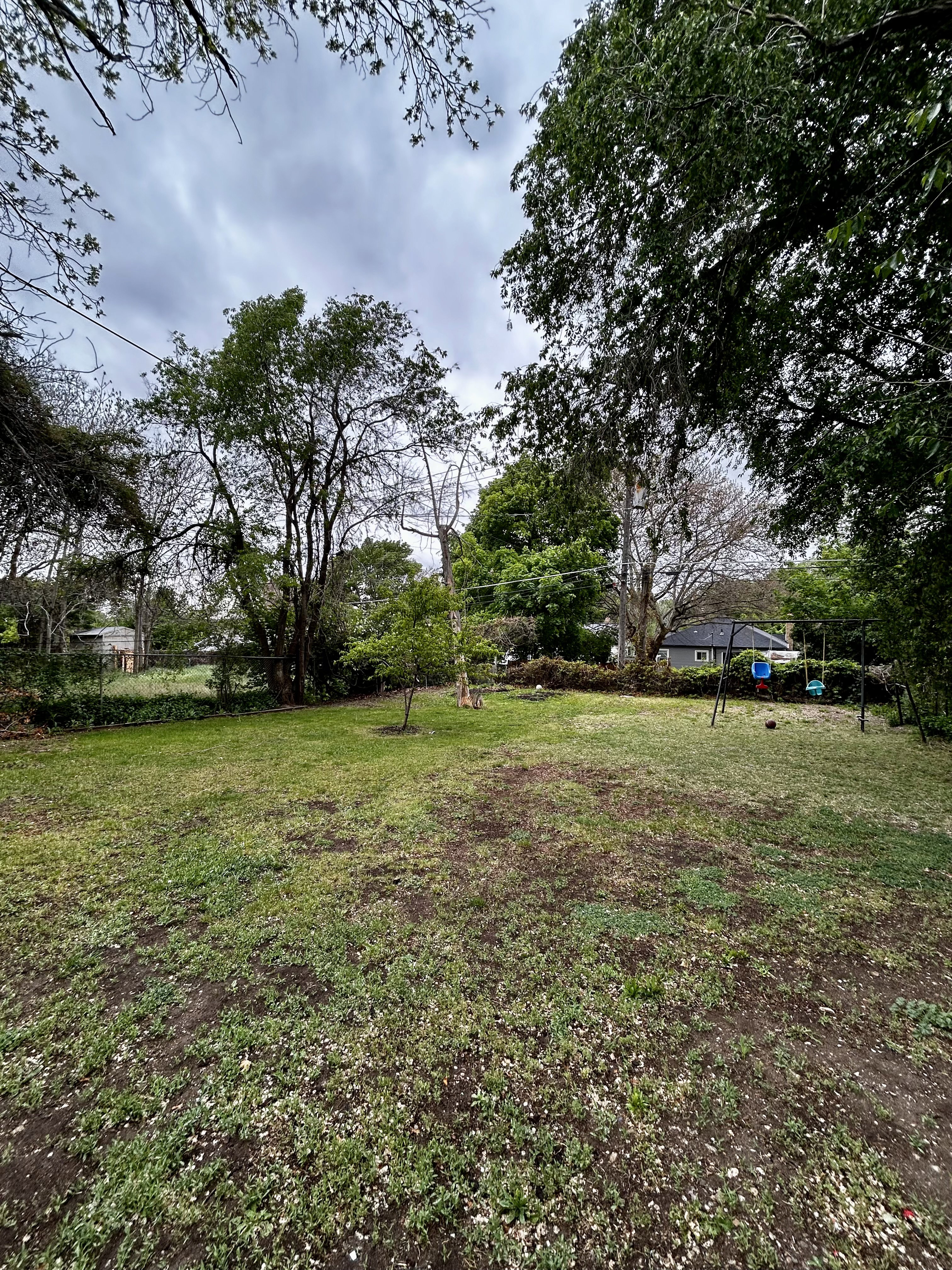 Expansive outdoor space featuring a large lawn area and mature trees providing natural shading
