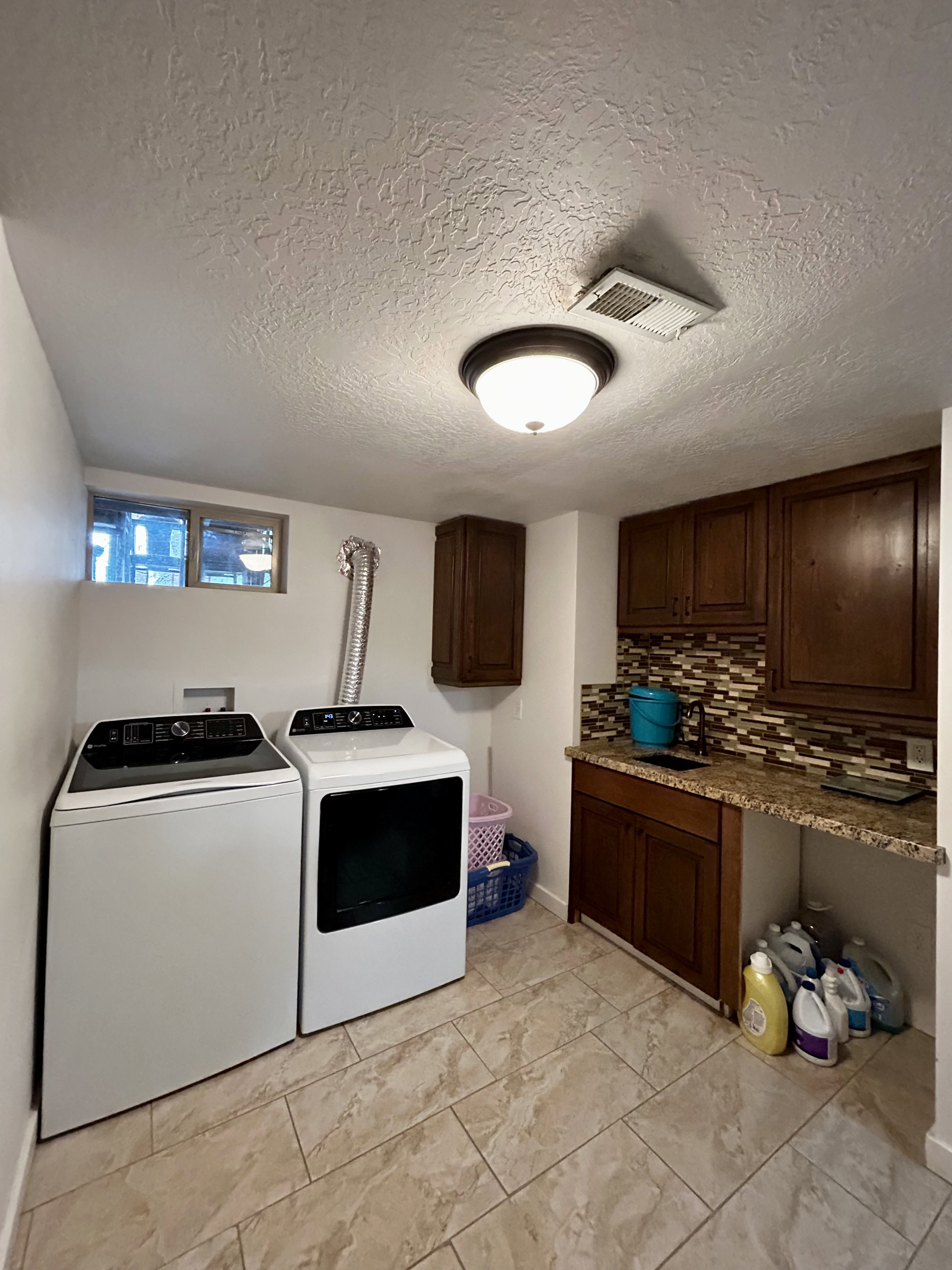 Dedicated laundry area featuring tile flooring, dark wood cabinetry, a built-in sink, tiled backsplash, and recessed lighting