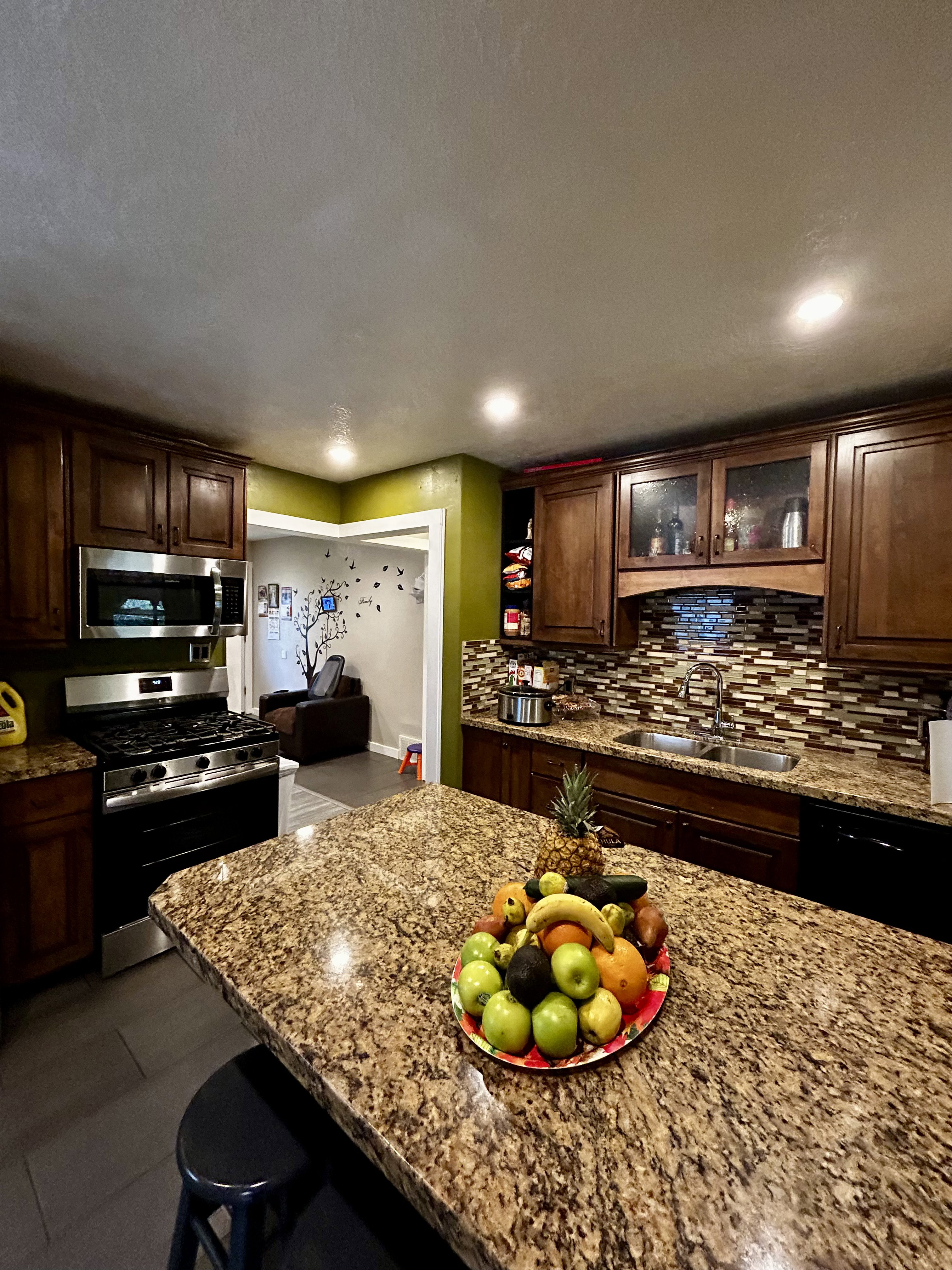 Kitchen featuring a large island with a stone-finish countertop, wood cabinetry, a stainless steel gas range, a stainless steel microwave, and a mosaic tile backsplash