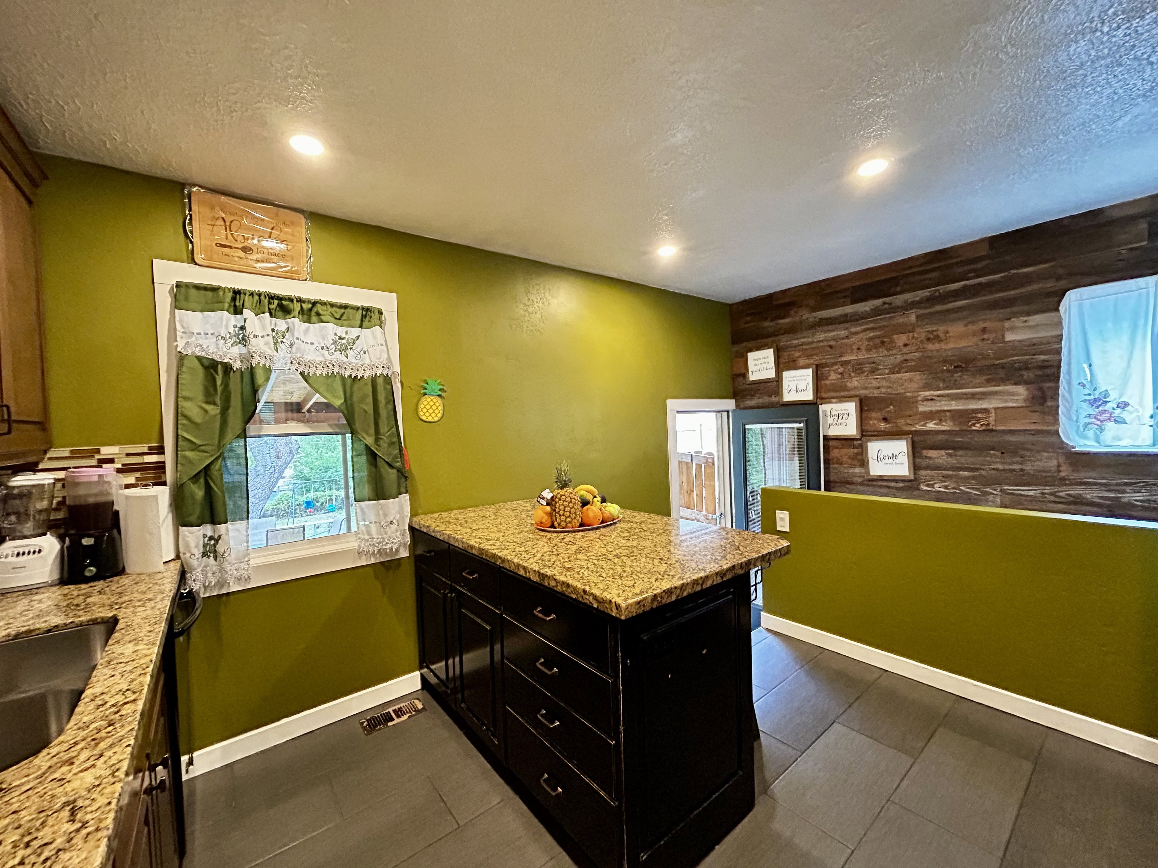 Kitchen featuring recessed lighting, a central island with a granite-style countertop, dark wood-finish cabinetry, and a wood plank accent wall