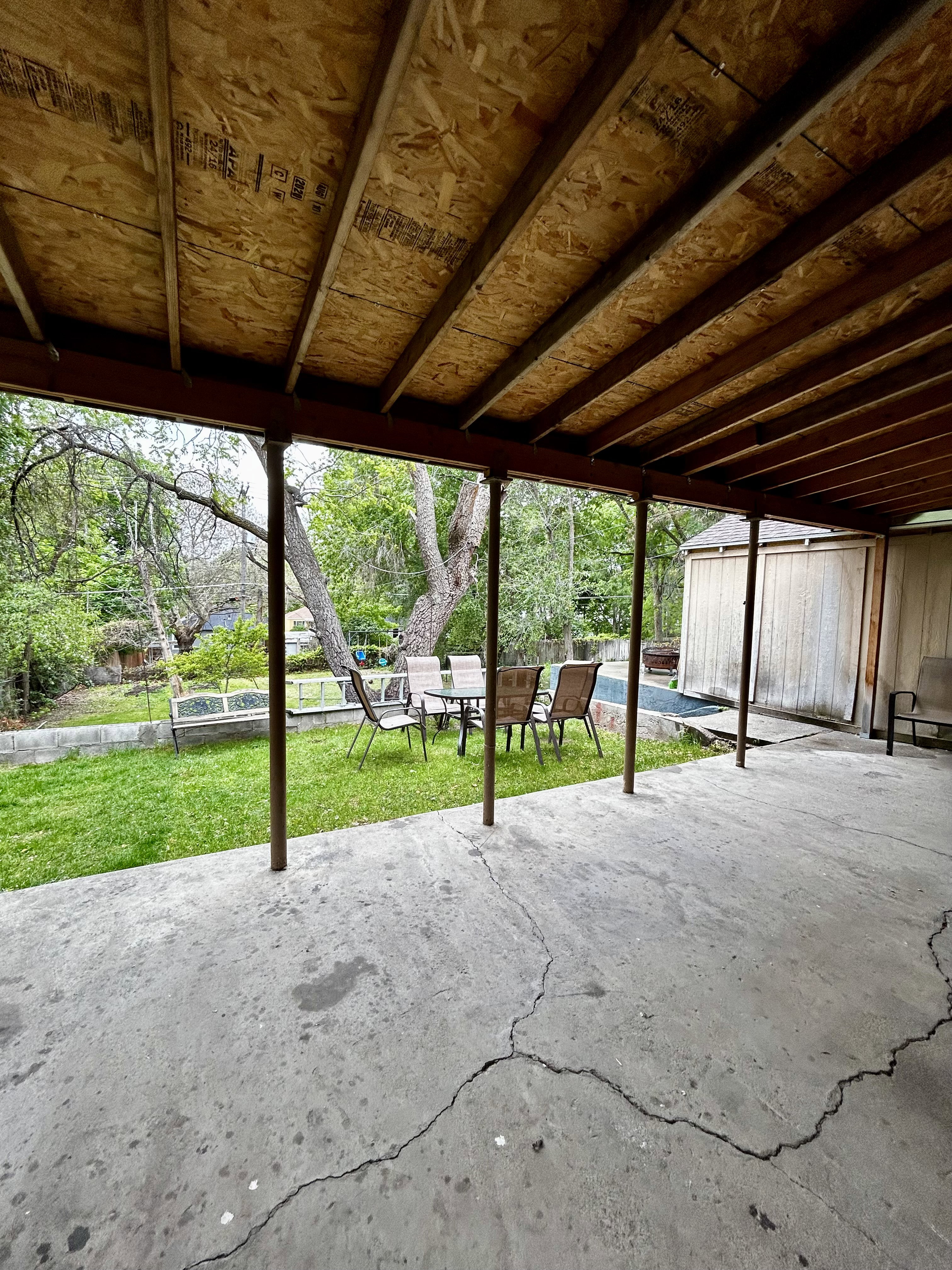 Covered patio space featuring an exposed plywood ceiling, supporting columns, and a concrete slab